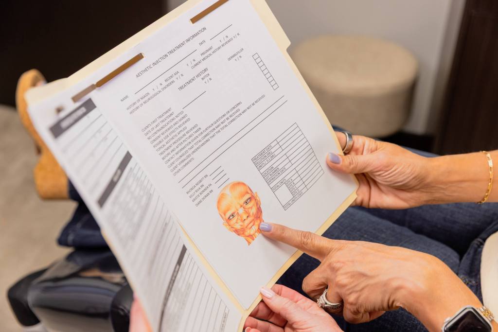 A Skin Boutique provider points to an image in a folder, helping a patient understand placement for her dermal fillers in Oakland County, MI.